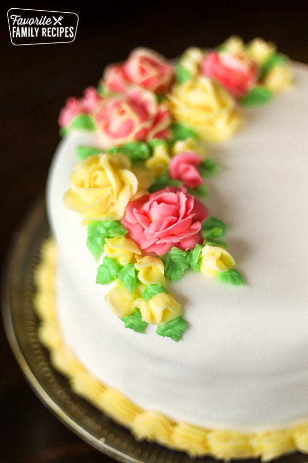 A round cake with white fondant and pink and yellow frosting flowers