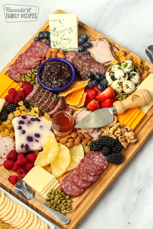 A wooden charcuterie board with jam, cheese, fruit, and slices of meat. 