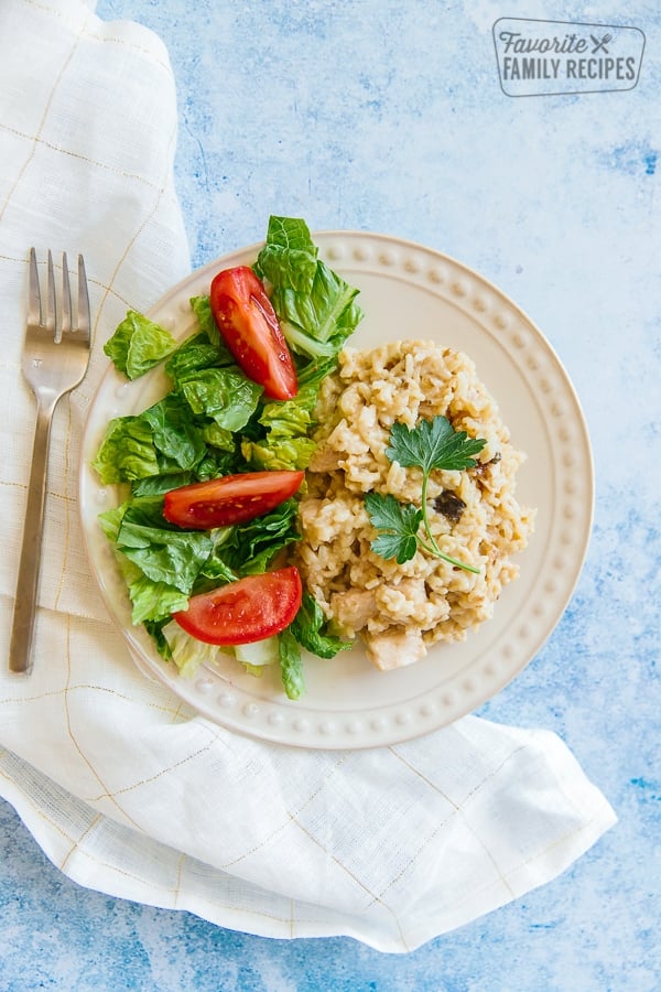Chicken casserole on a white plate with salad and tomato wedges on the side with a fork on the side of the plate.