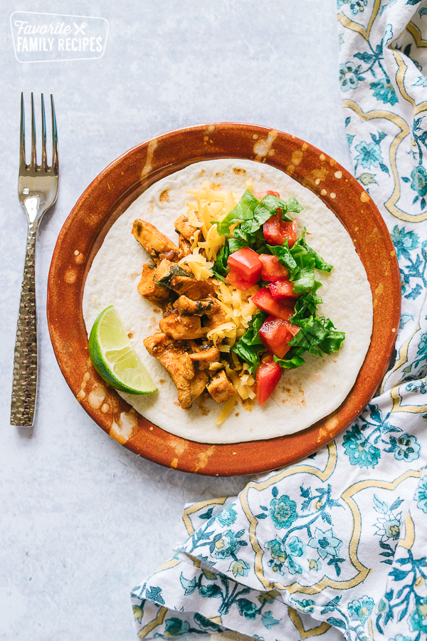 Chicken Taco on a plate with sliced tomatoes, lettuce, and cheese and a lime on the side