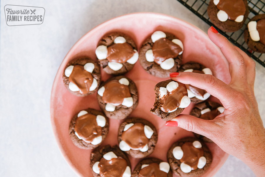 A chocolate marshmallow cookie being picked up from a pink plate full of cookies