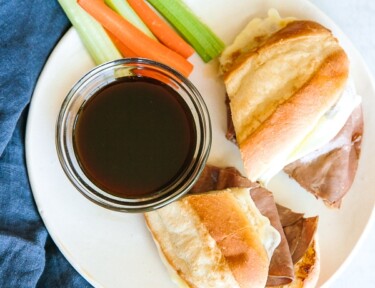 French Dip Sandwiches on a white plate with au jus and carrot and celery sticks