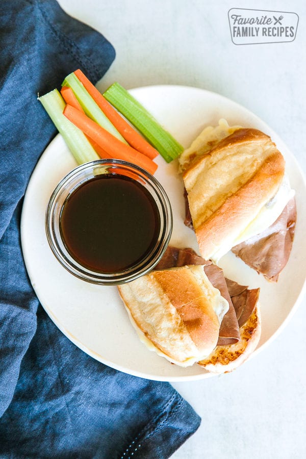 French Dip Sandwiches on a white plate with au jus and carrot and celery sticks