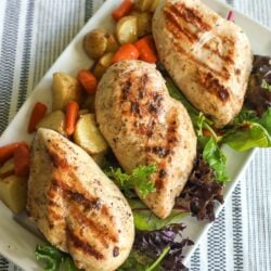 A tray of grilled chicken garnished with lettuce, red potatoes, and carrots