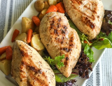 A tray of grilled chicken garnished with lettuce, red potatoes, and carrots