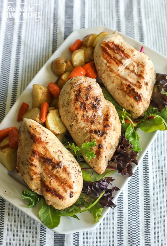 A tray of grilled chicken garnished with lettuce, red potatoes, and carrots