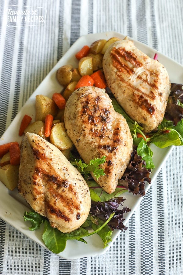 A tray of grilled chicken garnished with lettuce, red potatoes, and carrots
