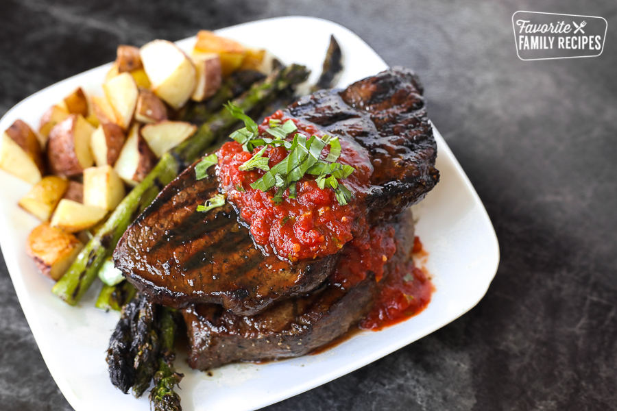 A landscape view of a square white plate with a grilled sirloin steak with tomato basil sauce on the side.