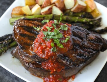 A grilled sirloin steak with tomato basil sauce on top and red potatoes on the side