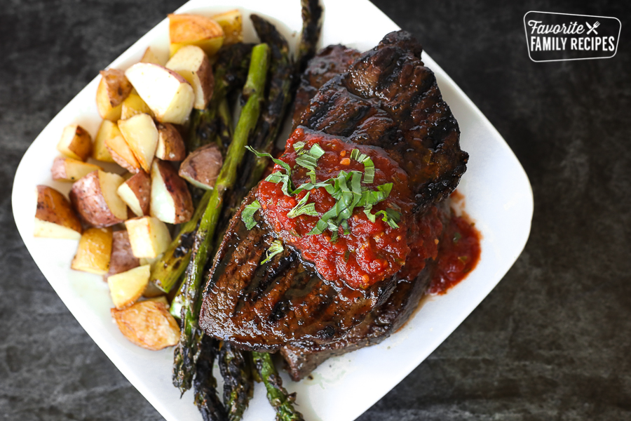 An overhead view of a sirloin steak with tomato basil sauce, asparagus, and roasted potatoes on the side