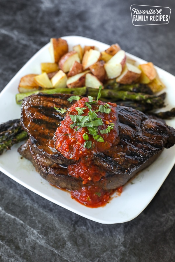 A grilled sirloin steak with tomato basil sauce on top and red potatoes on the side.