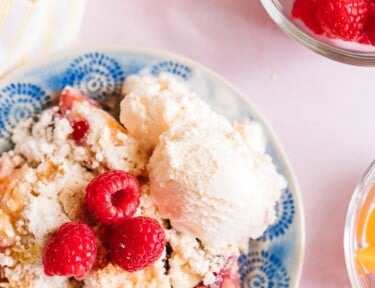 Raspberry Peach Cobbler served on a blue plate with ice cream on the side