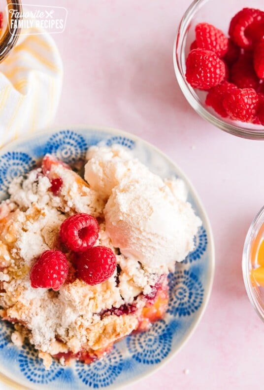 Raspberry Peach Cobbler served on a blue plate with ice cream on the side