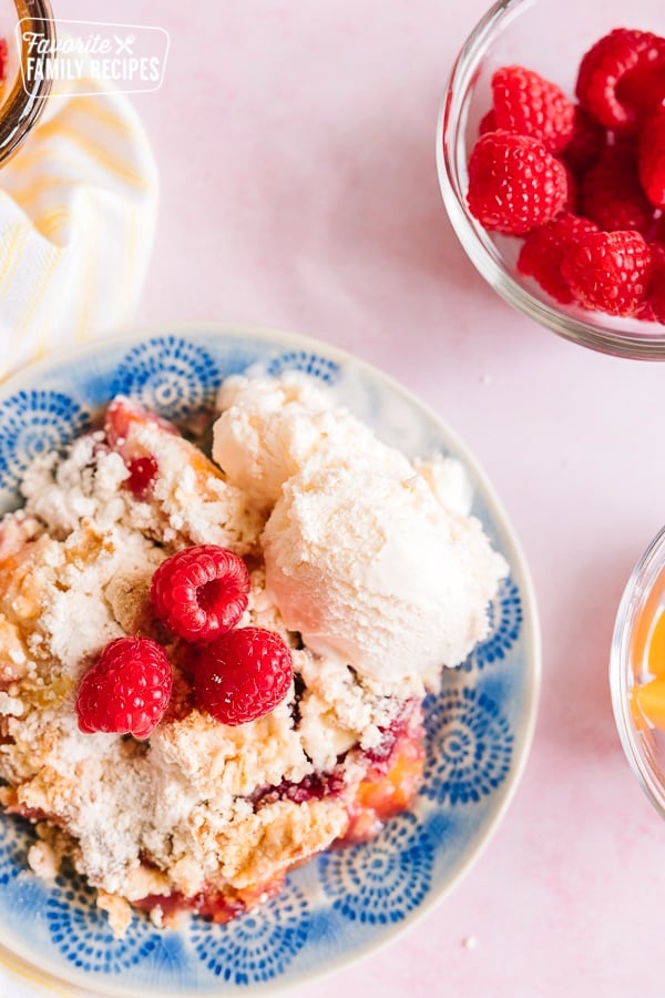 Raspberry Peach Cobbler served on a blue plate with ice cream on the side