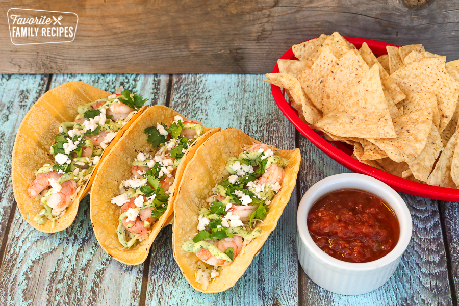 Shrimp tacos on a board with chips and a cup of salsa to the side