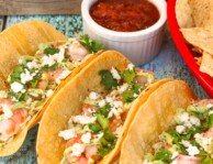 Three shrimp tacos with salsa and chips on the side