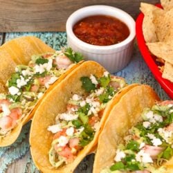 Three shrimp tacos with salsa and chips on the side