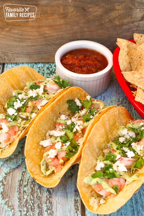 Three shrimp tacos with salsa and chips on the side