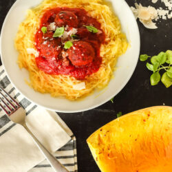 A bowl of spaghetti squash with red sauce and meatballs over the top next to a roasted spaghetti squash