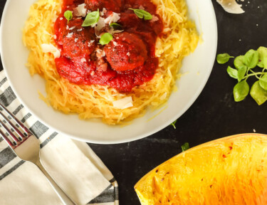 A bowl of spaghetti squash with red sauce and meatballs over the top next to a roasted spaghetti squash