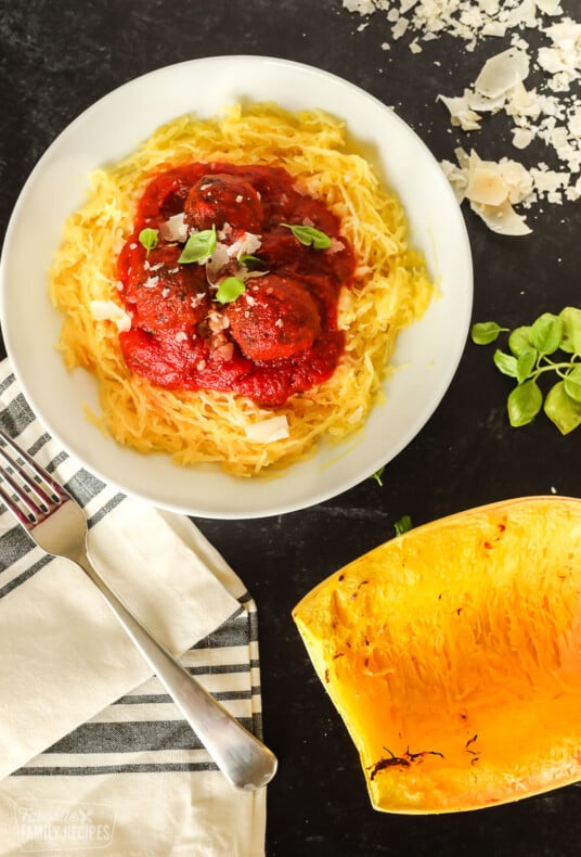 A bowl of spaghetti squash with red sauce and meatballs over the top next to a roasted spaghetti squash