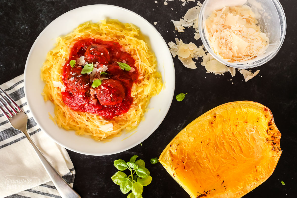 A bowl of spaghetti squash, a half of a squash, and a bowl of parmesan cheese on a table.