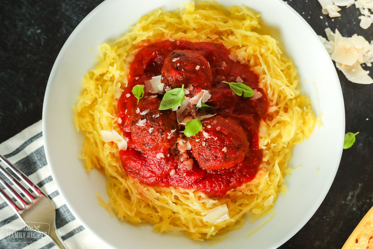 A close up of a bowl of spaghetti squash with sauce, meatballs, parmesan cheese, and fresh basil.