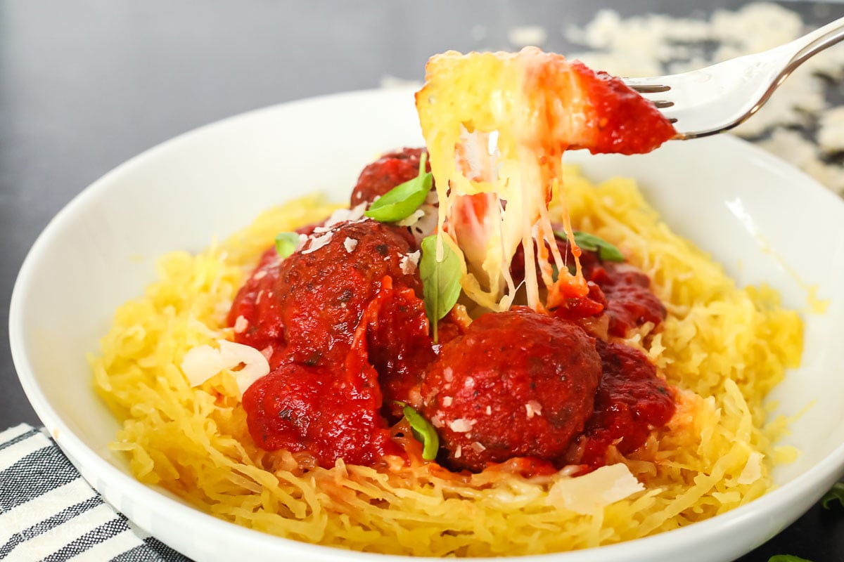 Spaghetti squash being pulled up from a bowl showing cheese pulling from the fork.