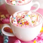 Two white mugs filled with Unicorn Hot Chocolate topped with mini marshmallows and sprinkles