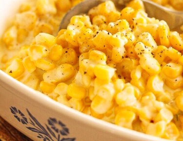 Slow Cooker Creamed Corn in a white casserole dish with a serving spoon scooping out corn