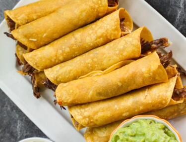 A platter filled with shredded beef taquitos