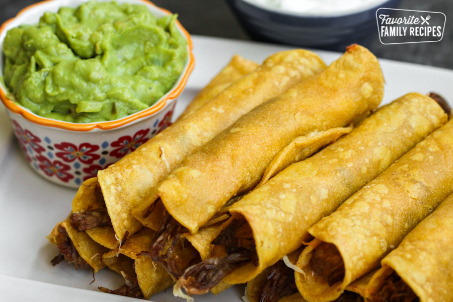 A close up look at a plate of beef taquitos with a bowl of guacamole on the side