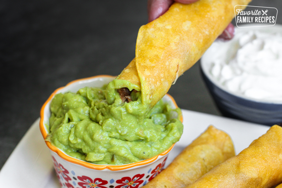 A shredded beef taquito being dipped into a bowl of guacamole