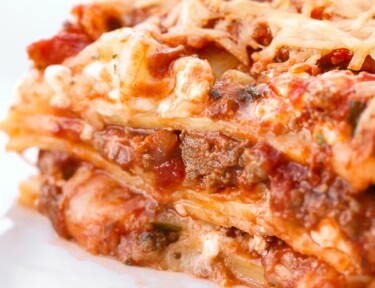 A piece of lasagna viewed close up with layers of lasagna noodles, meat, cheese, and tomatoes