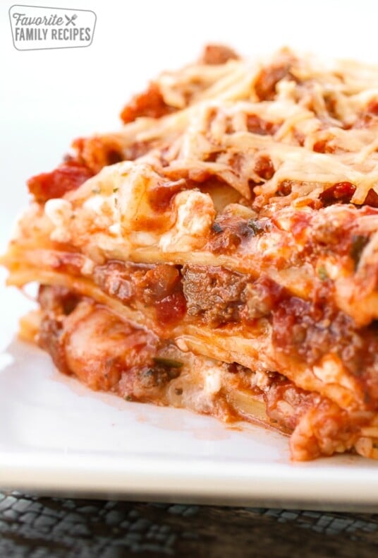 A piece of lasagna viewed close up with layers of lasagna noodles, meat, cheese, and tomatoes