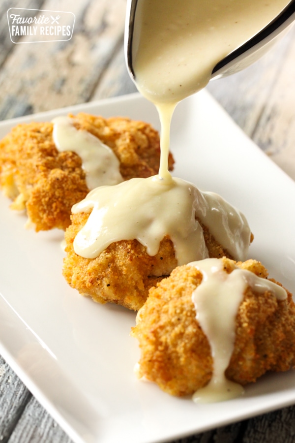 Chicken Cordon Bleu Sauce being poured on three pieces of chicken cordon bleu on a plate