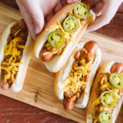 A chili cheese dog being picked up from a tray of chili dogs