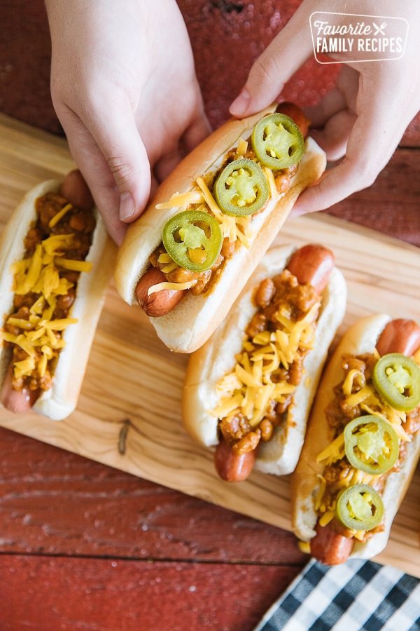 A chili cheese dog being picked up from a tray of chili dogs