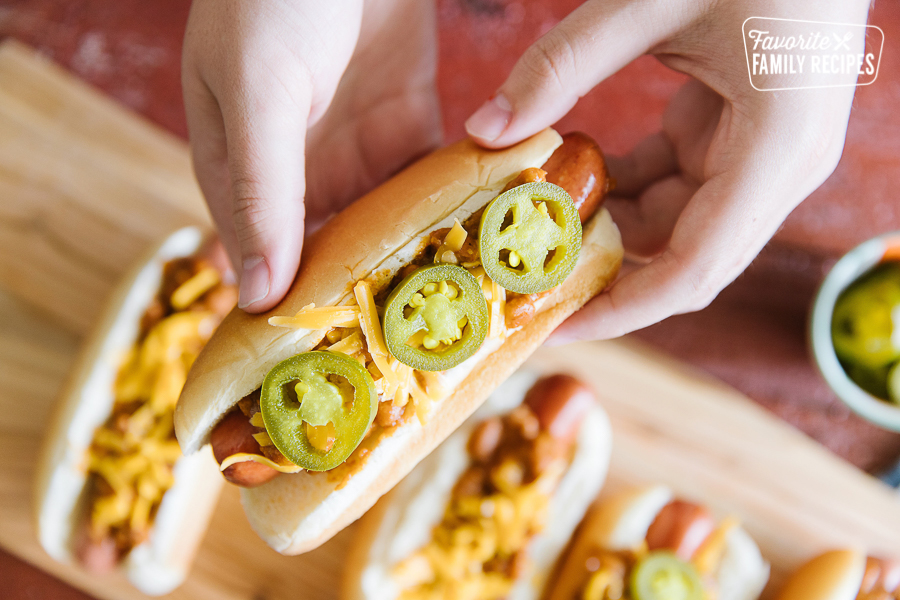 A chili cheese dog with jalapeños held up over a tray of chili cheese dogs.