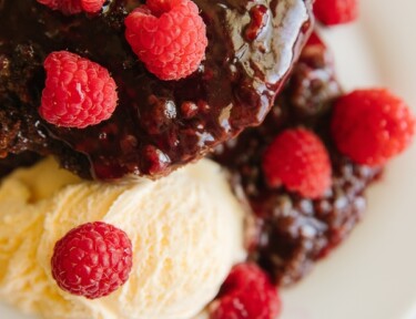 A serving of Chocolate Raspberry Cake with ice cream and raspberries as a garnish