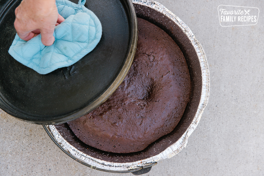 The lid of a dutch oven is being lifted to reveal a chocolate raspberry cake on the inside