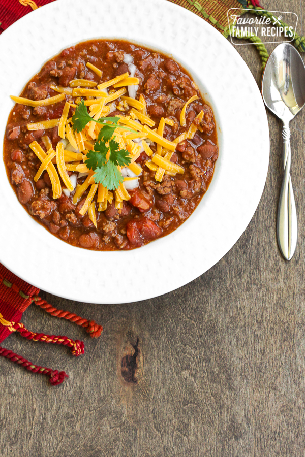 A bowl of chili with shredded cheese on top with a spoon on the side. 