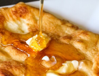 Honey being poured over a piece of fry bread with butter on top