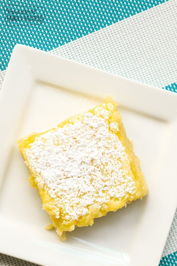 A square white plate with a lemon bar on it.