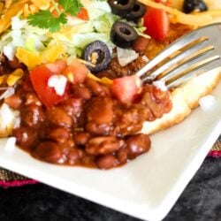 A navajo taco on a plate with a fork cutting into it