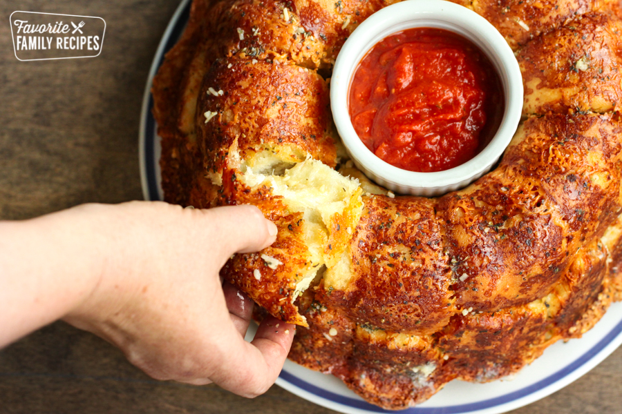 A piece of Parmesan Pull Apart bread being pulled from a bread ring