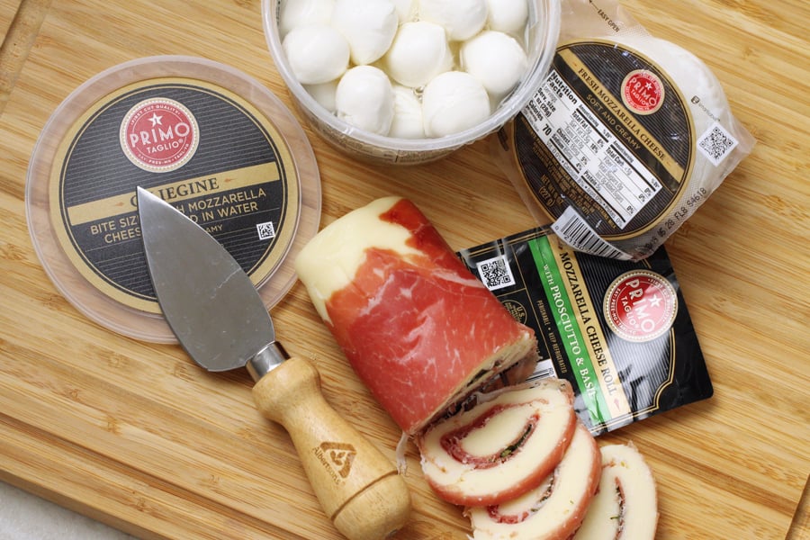 Mozzarella balls, packaged mozzarella, and a cheese roll on a cutting board.