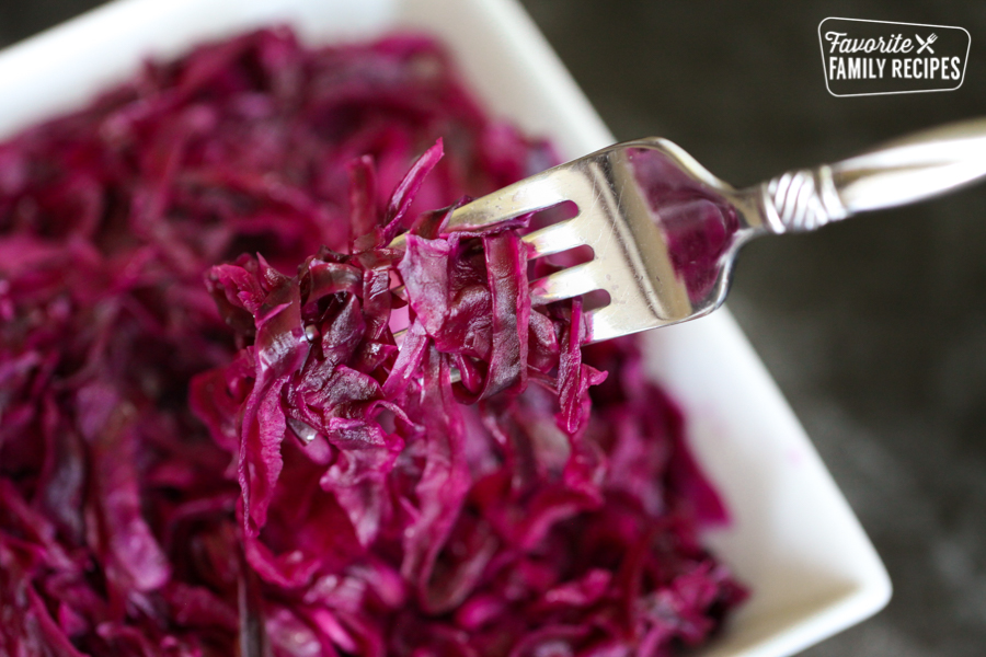 A fork lifting a bite of Danish Red Cabbage or Rodkal from a white bowl