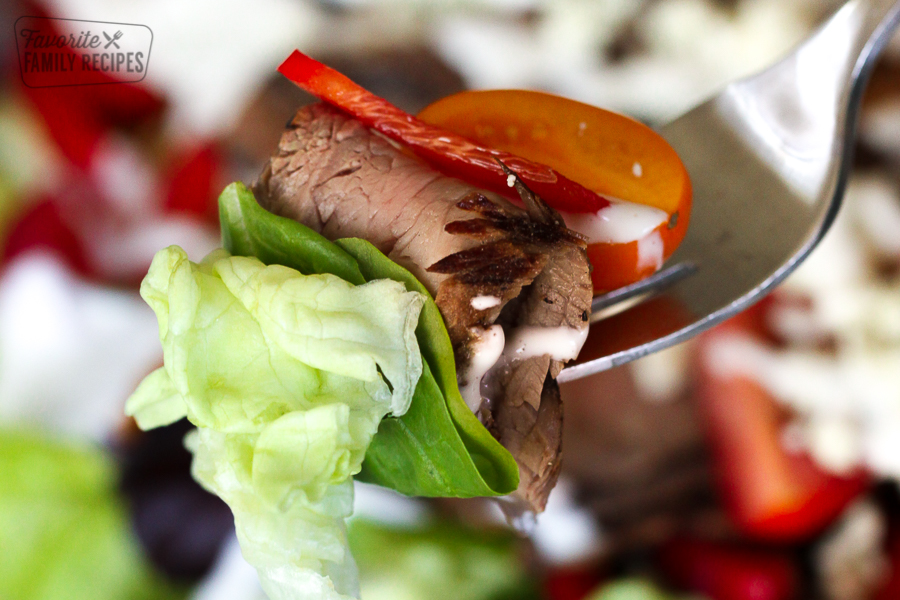 A fork with steak salad - steak, lettuce, tomato, and pepper on it