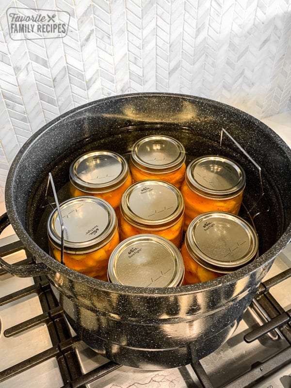 Glass jars filled with peaches in a water bath canner.